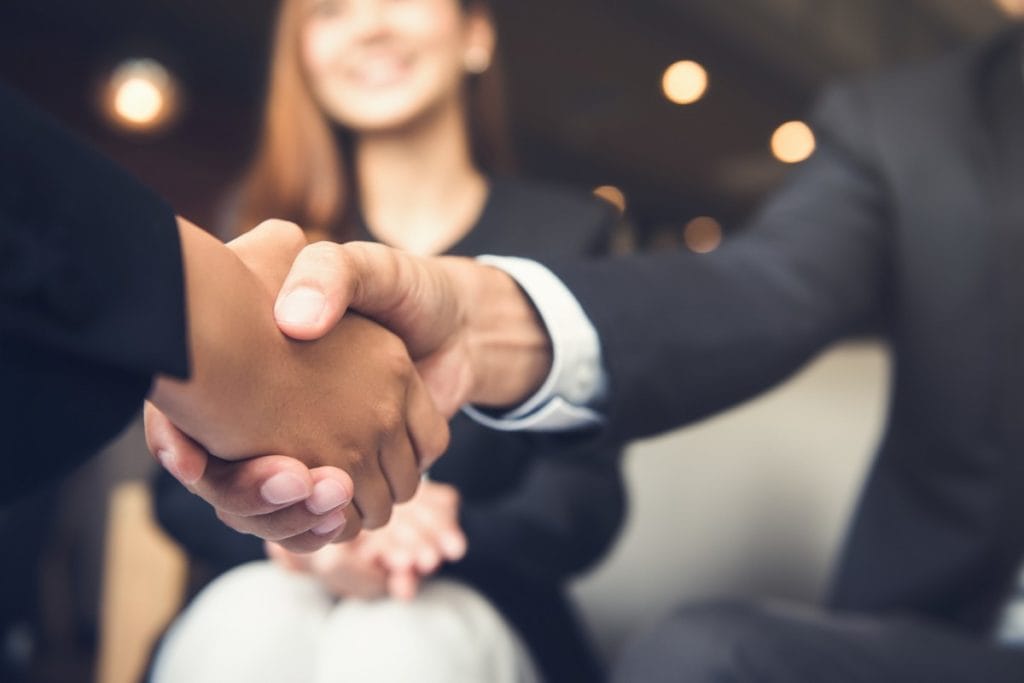 2 people wearing suits shaking hands as a sign of etiquette