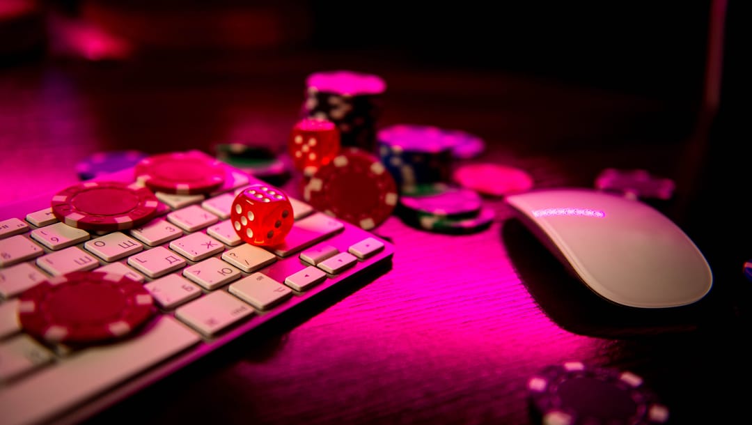 Dice and gambling chips on a keyboard and mouse with a red light.