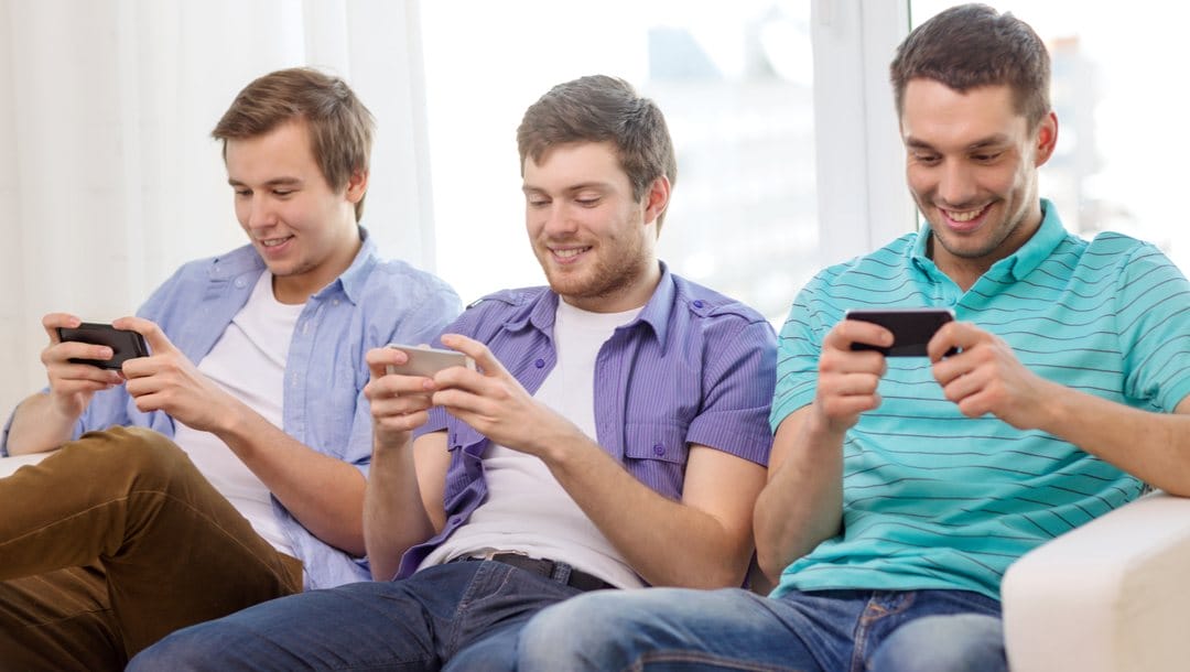Three friends sitting on a couch using their mobile phones.