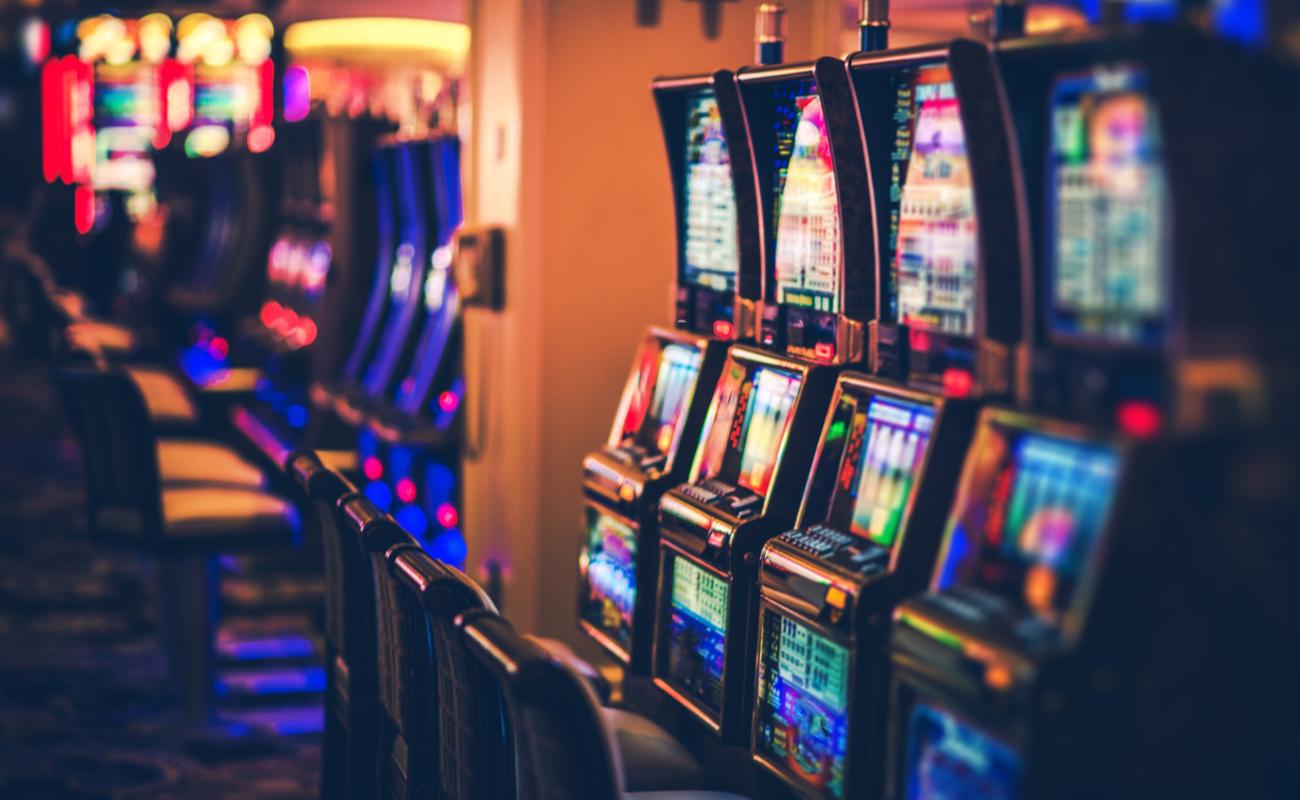 A row of casino slots with lots of different color lights in a dimly lit casino