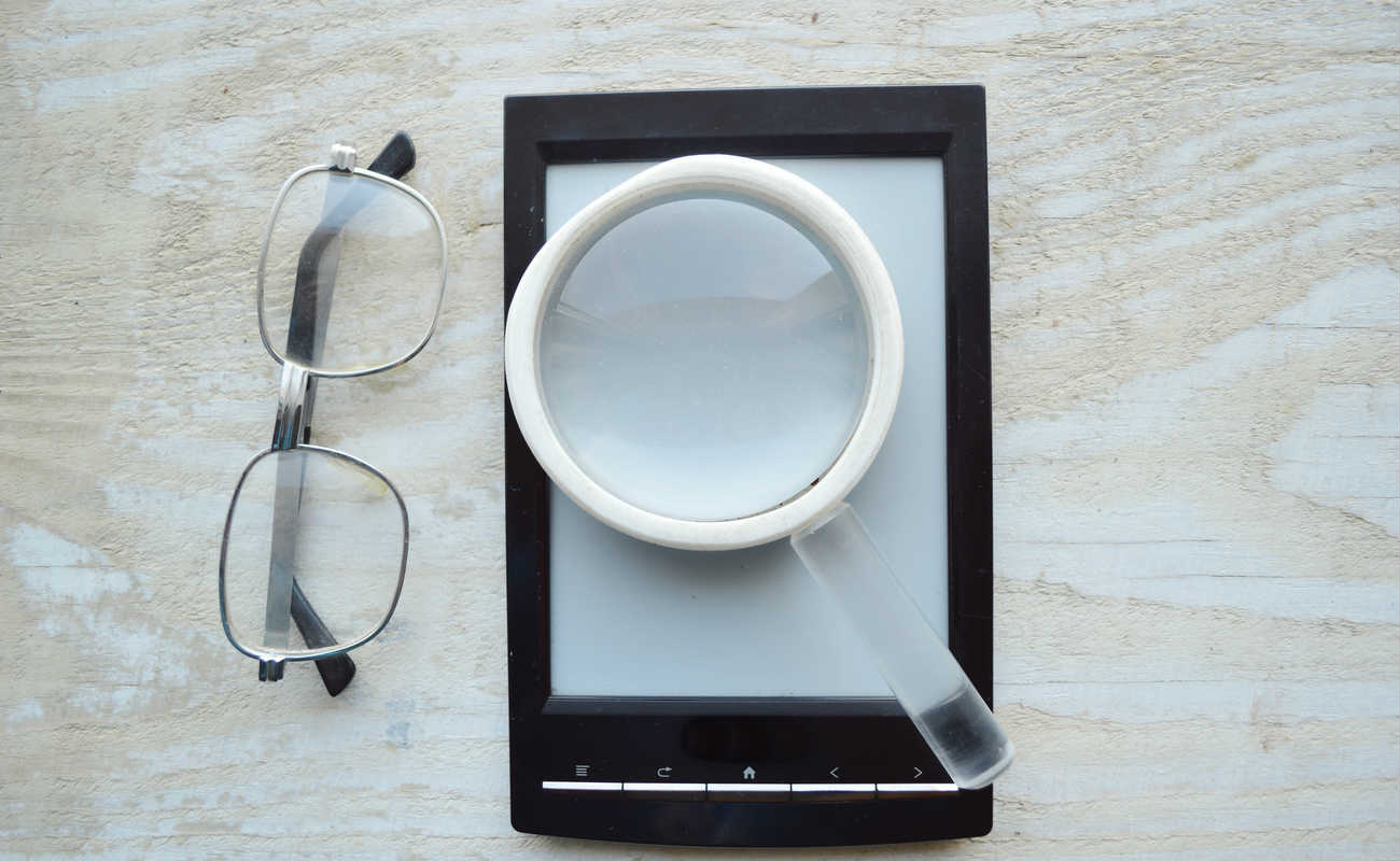 black ebook, reading glasses, notepad and magnifying glass