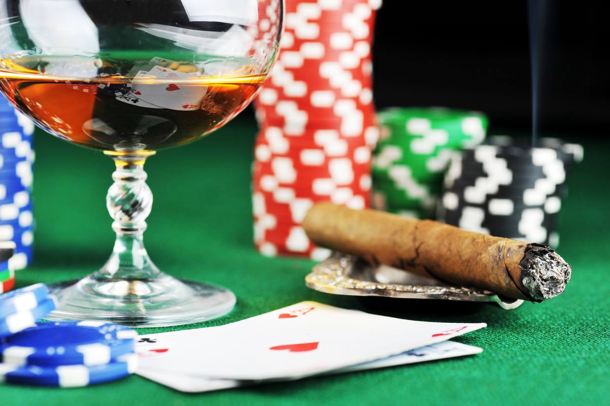 Cigar, poker chips, whiskey glass and playing cards on a green casino table