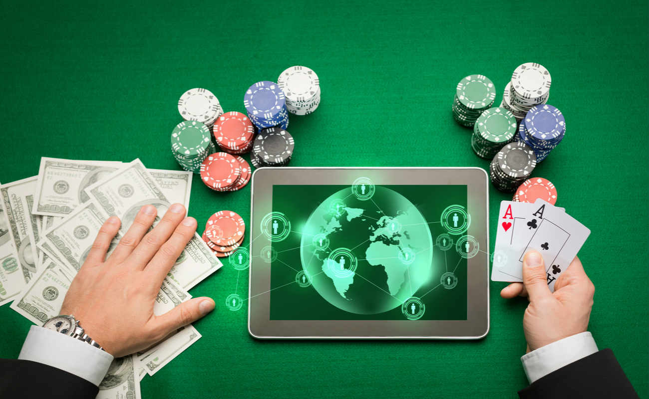 poker player holding playing cards, chips and earth projection with users icons on tablet pc