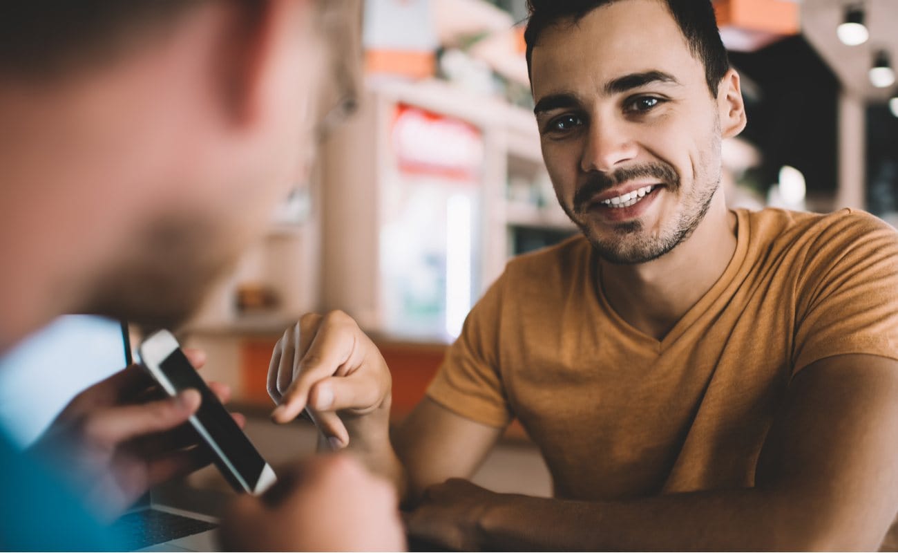 Back view of man holding cellphone and showing friend something