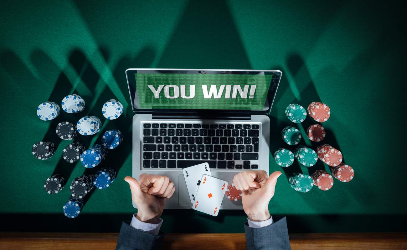 Man thumbs up playing online poker with laptop on a green table with chips, top view