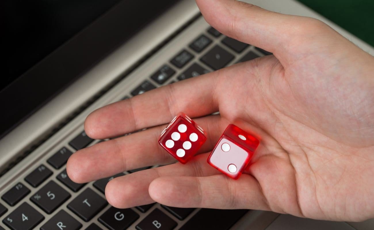 Hand holding two red dice above keyboard