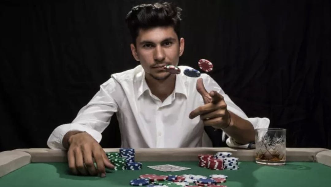 A person in a white shirt sits at a poker table and throws chips.