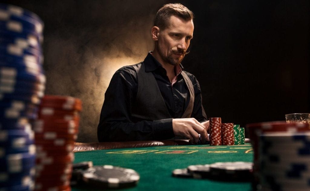 Confident Man Sitting Behind Poker Table With Cards And Chip