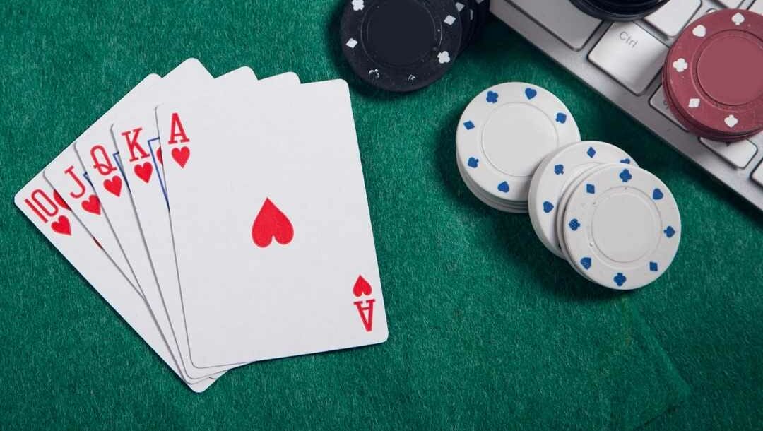 A royal flush poker hand sits next to a keyboard with poker chips on it