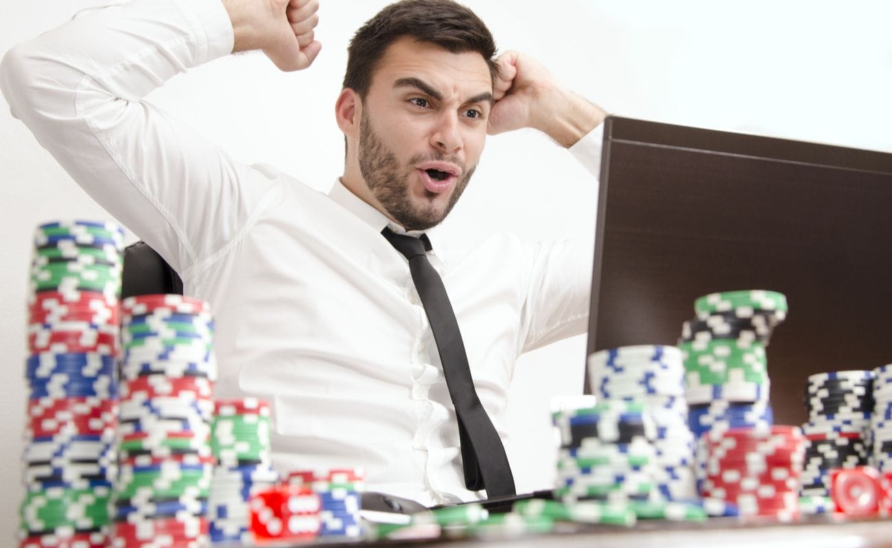 Man showing excitement while looking at laptop with poker chips on the table