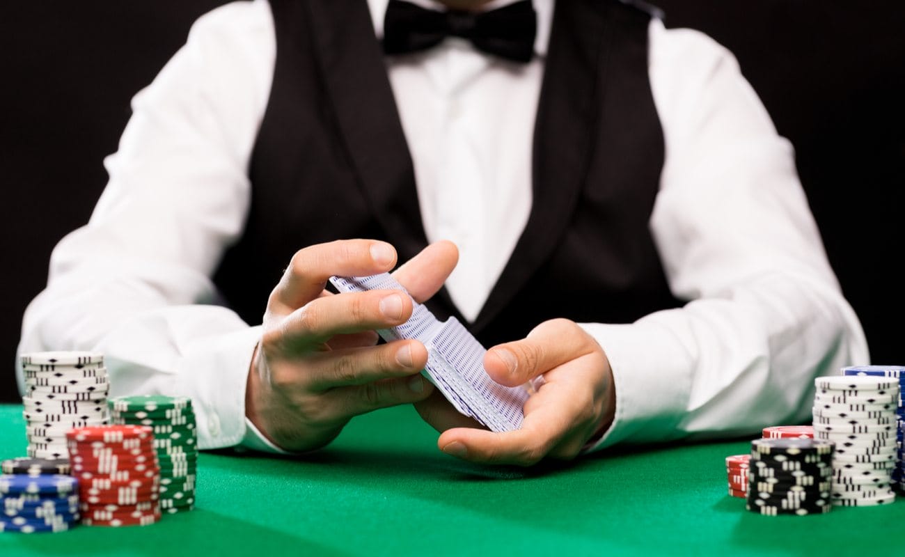 A casino dealer shuffles cards with piles of chips on the table in front of them