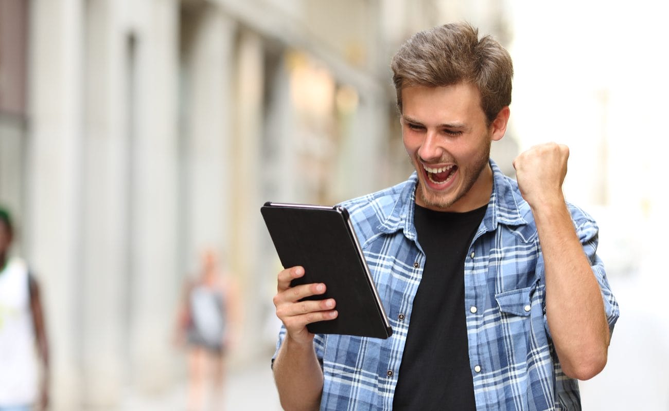 A young man raises his fist in victory after winning a mobile game.