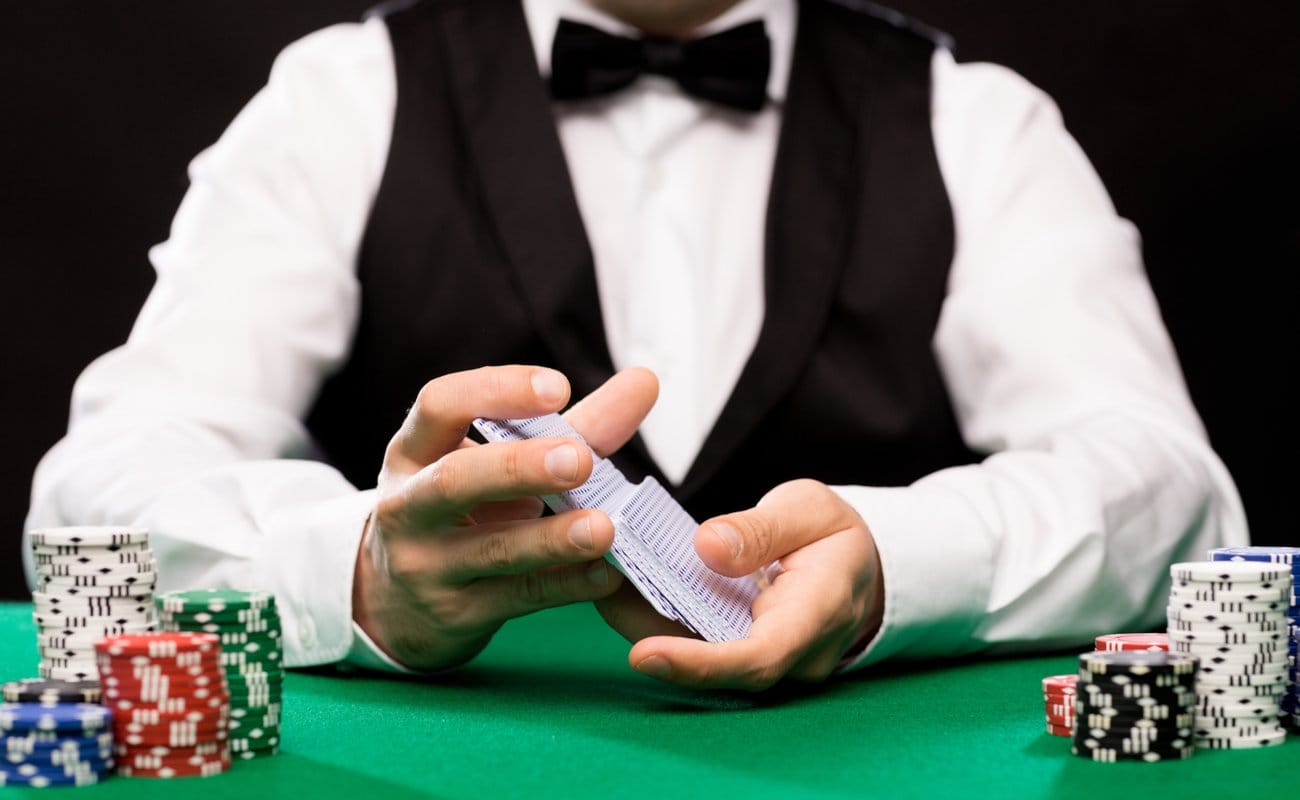 Casino dealer shuffles playing cards at a green felt table with chip stacks.