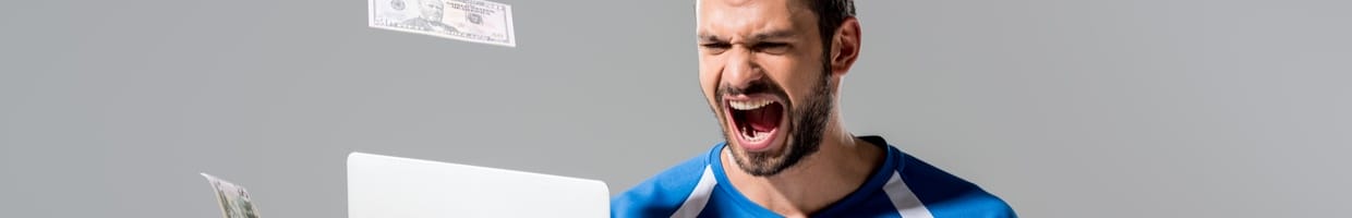 A sports fan holding a laptop and a soccer ball while money falls around him.