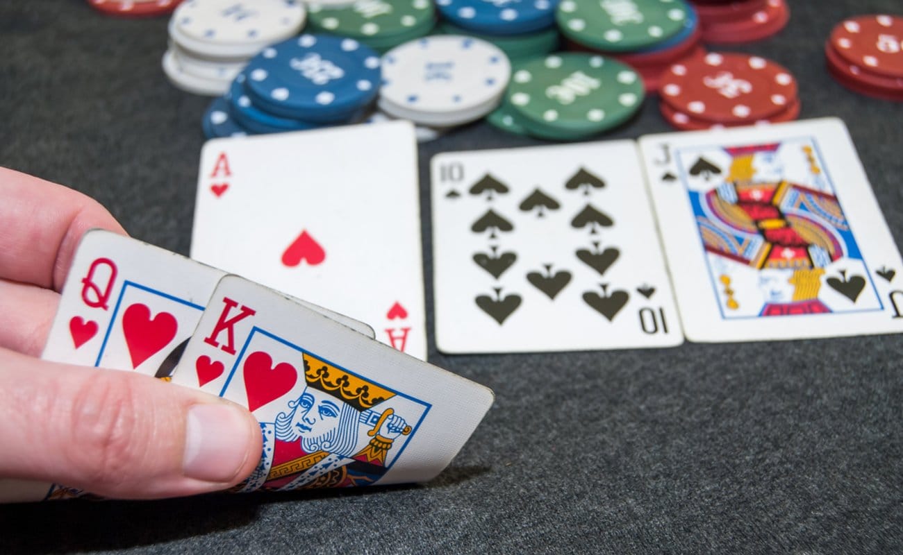 A hand reveals a king and queen, with other face-up playing cards in the background.
