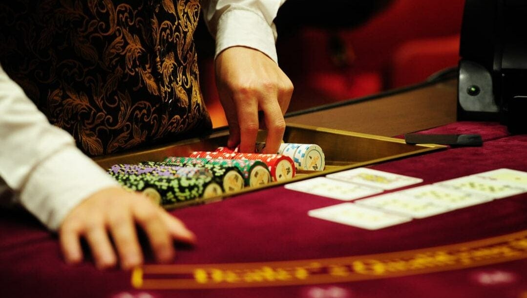 A poker dealer’s hands prepare chips at a red casino table with playing cards and casino chips.