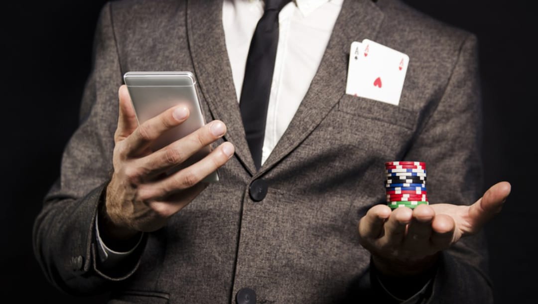 The gambler holds a mobile phone in his right hand and a chip in his left.