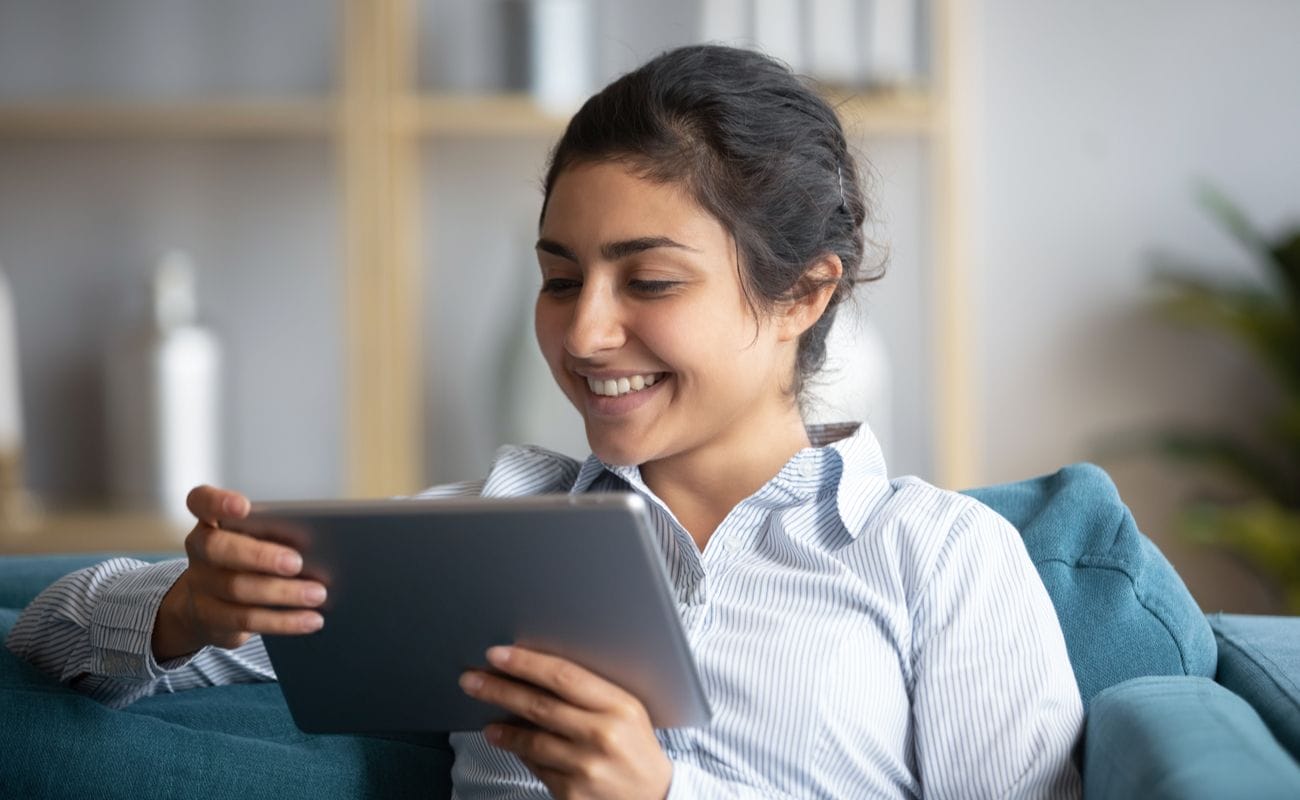 A young woman sits on her couch playing games on her tablet.