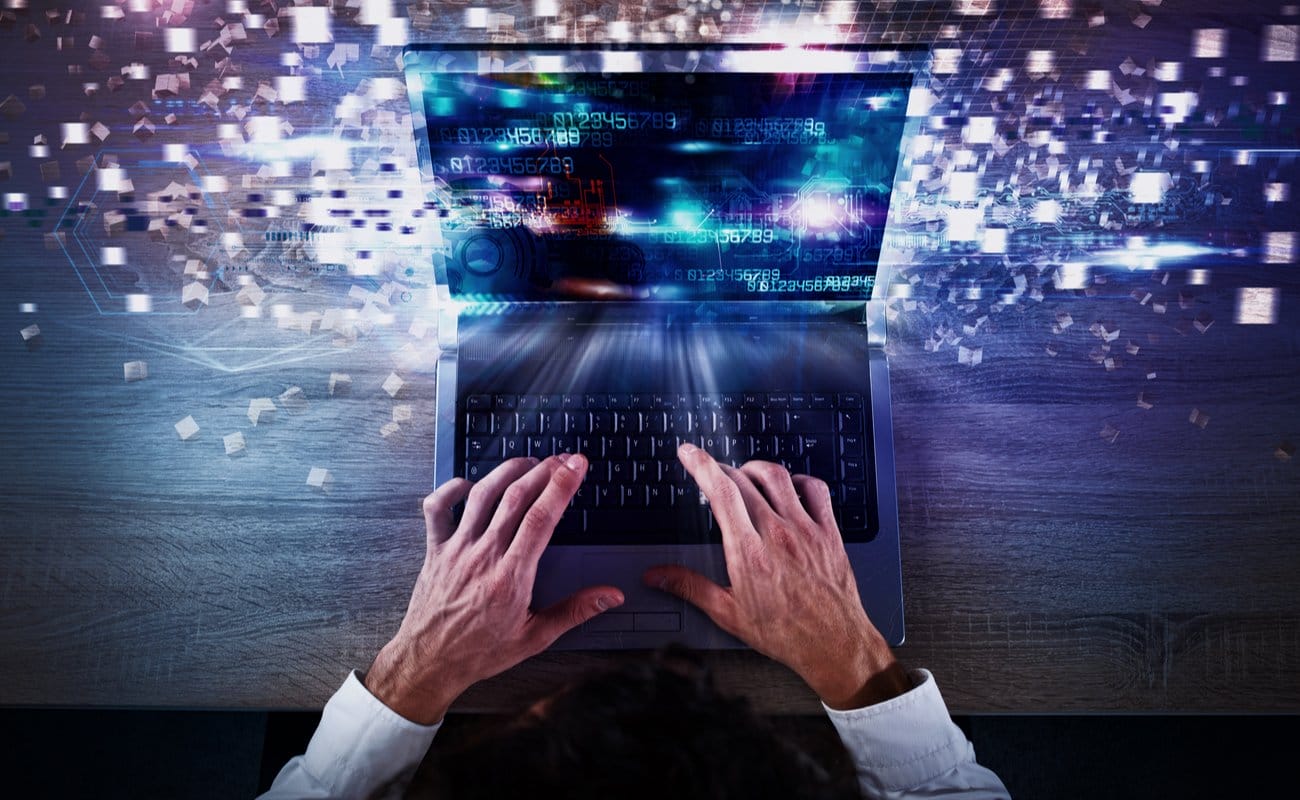 man typing on a laptop with scattered symbols flying from the screen to imply a speedy connection - Improve your laptop's performance.