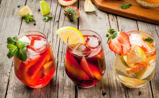 Three mocktails displayed on a wooden table with cut-up fruit.