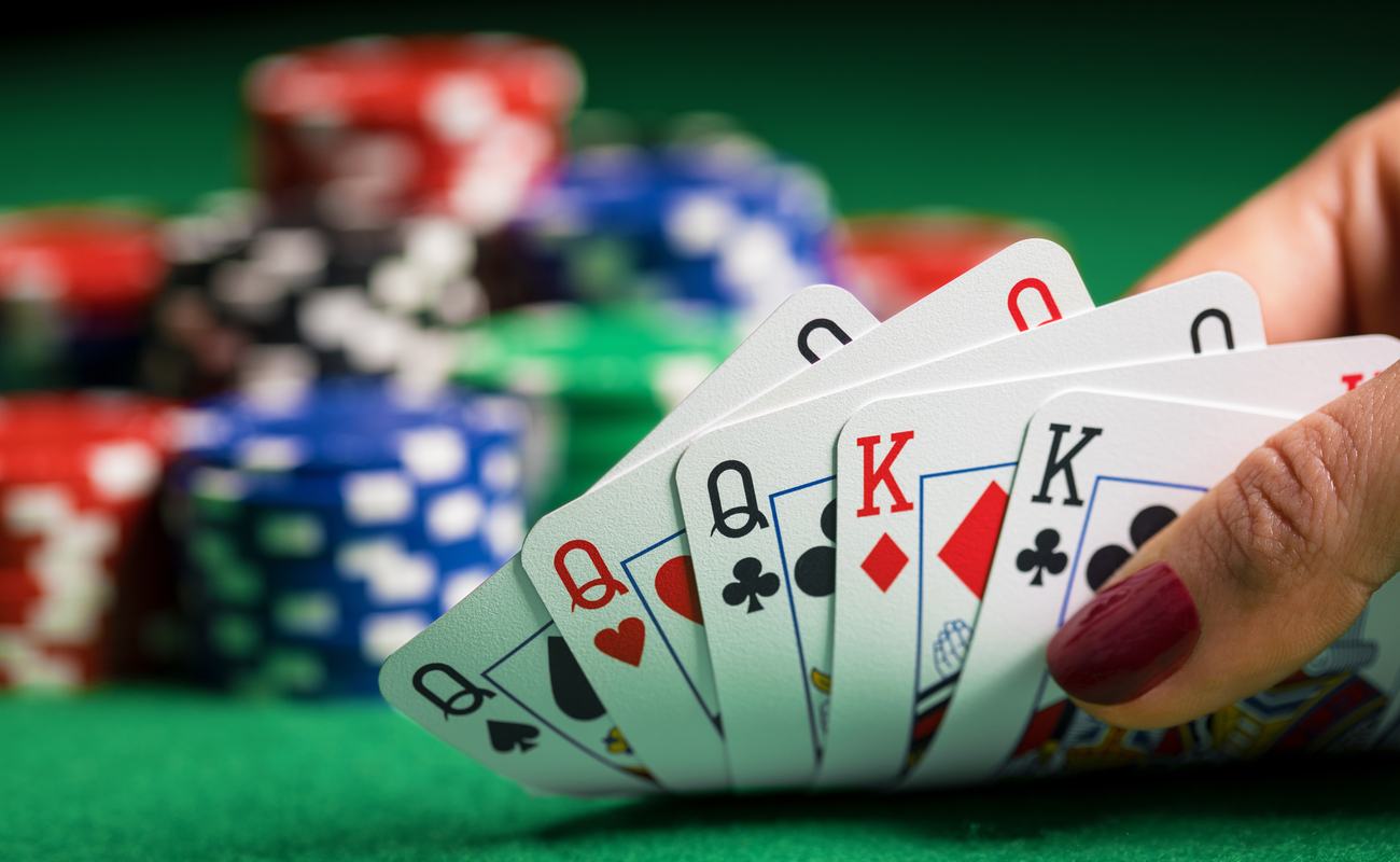 A woman holding playing cards in her hand on a green felt table with poker chips.