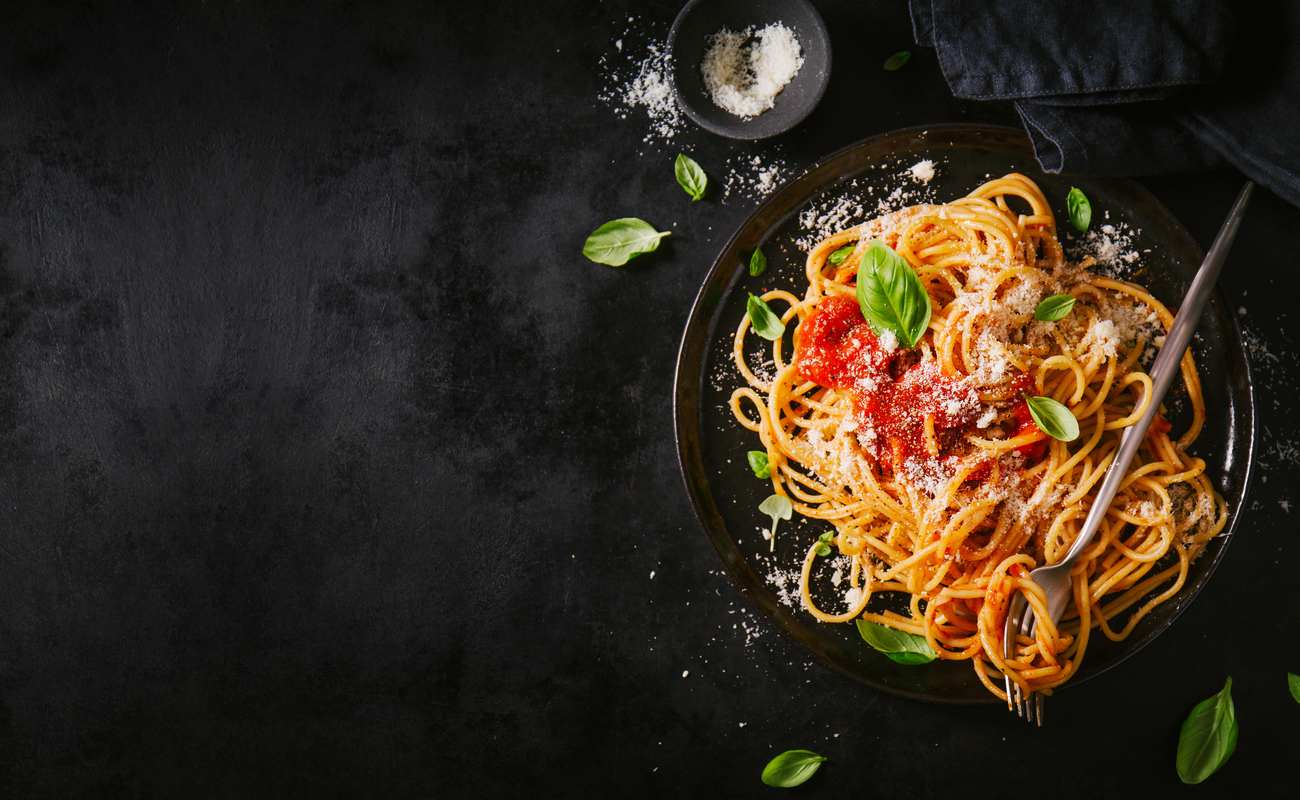Plate of pasta against a black background with a bowl of salt next to it.