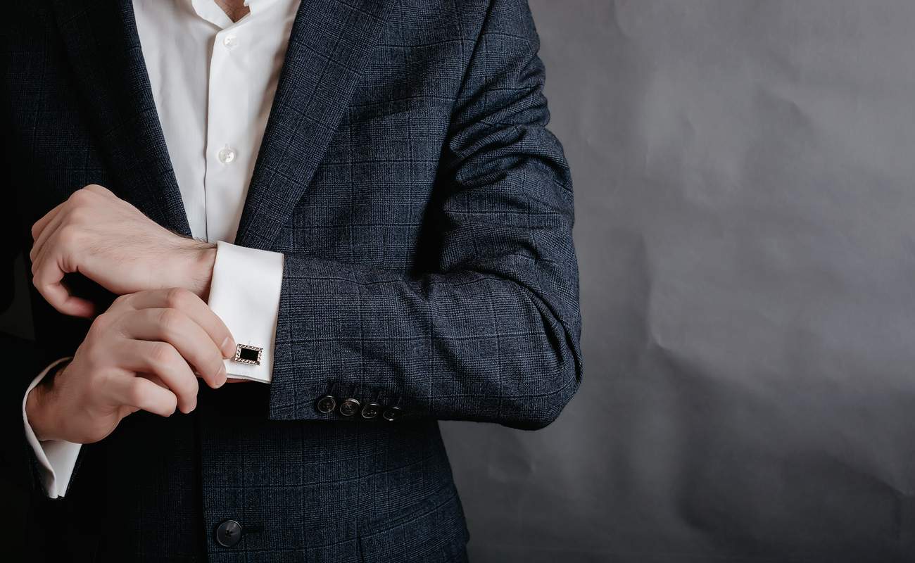 Man in a tuxedo adjusting the cufflinks on one sleeve.