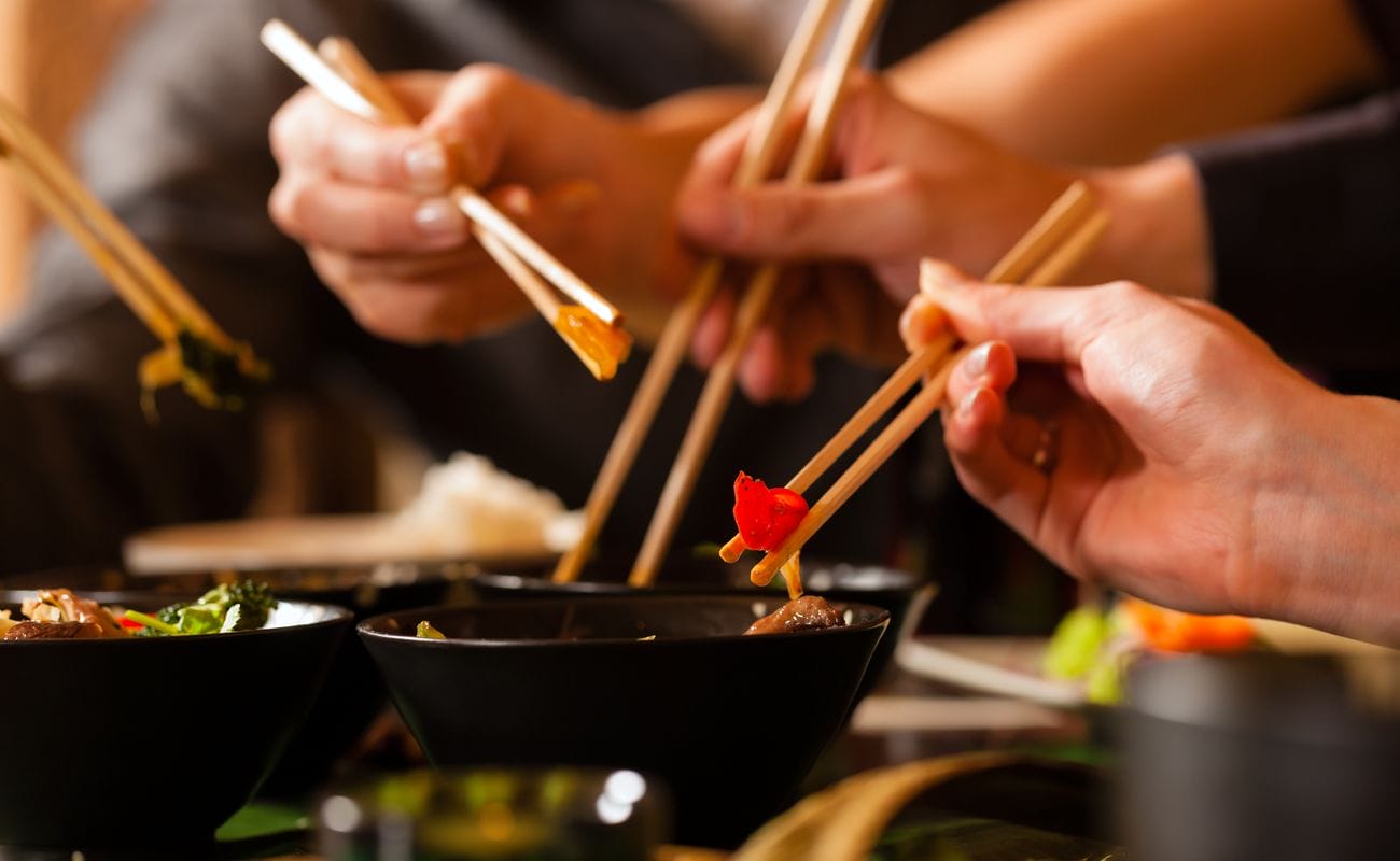 People eating out of bowls with chopsticks at an Asian restaurant.