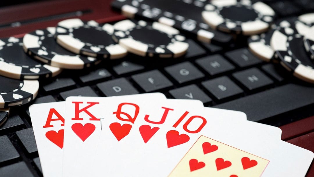 A royal flush sitting on a keyboard surrounded by poker chips.