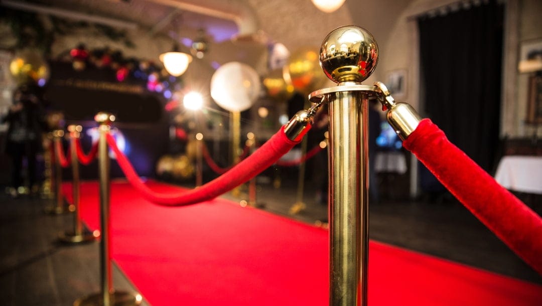 Celebrity red carpet event with gold stanchions and red ropes leading to a well-lit area, creating an elegant and glamorous atmosphere.