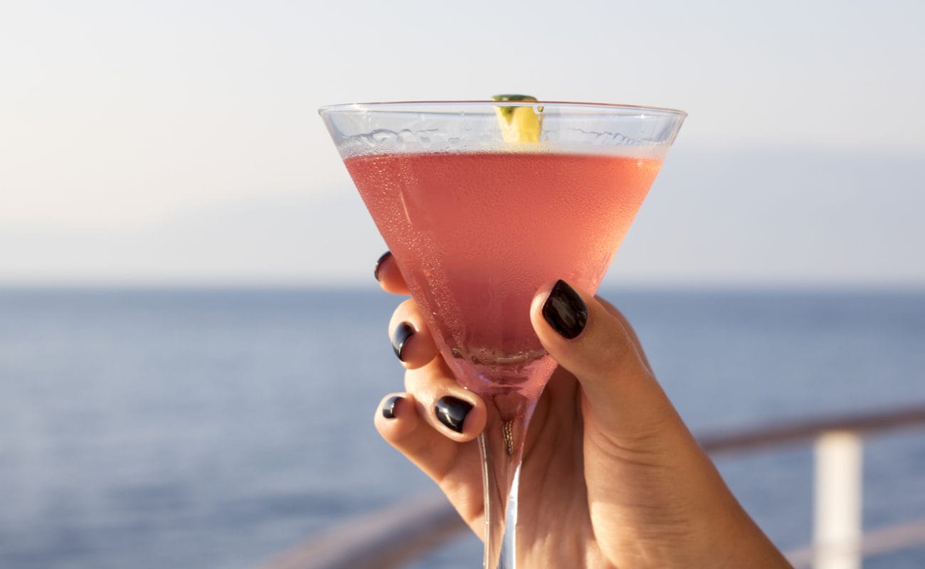 A woman’s hand holds a cocktail drink on the deck of a cruise ship.