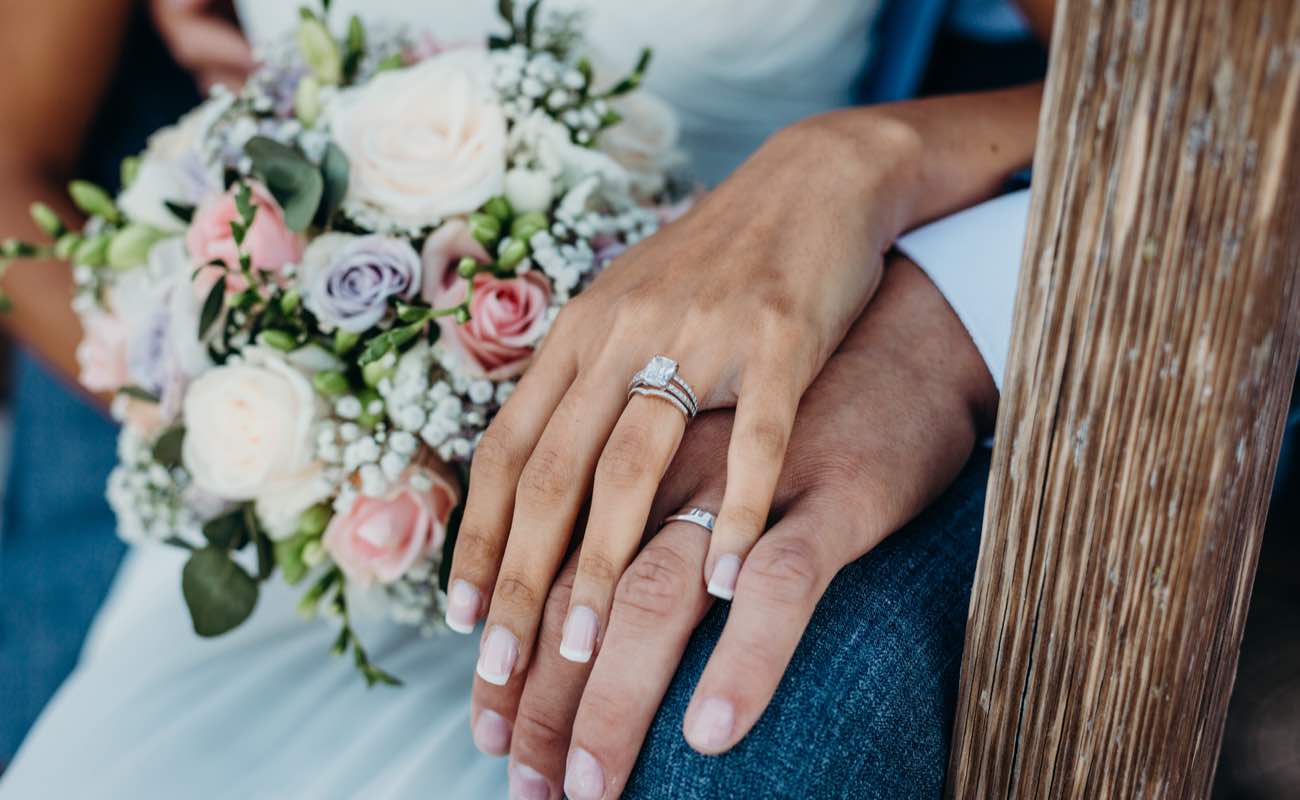 Close-up of a wedding couple’s hands and a bouquet of flowers.