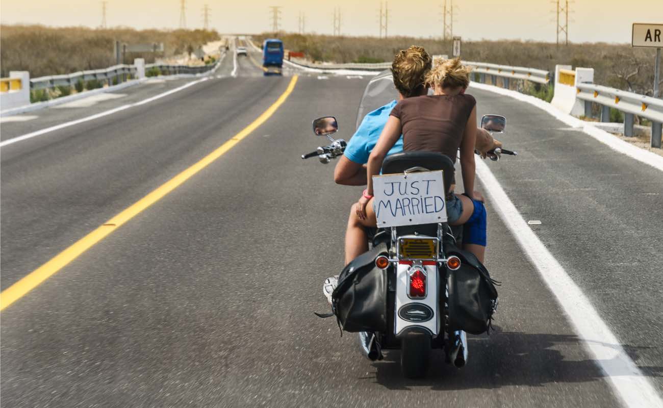 Couple riding on a motorbike on the highway with a “Just Married” sign.