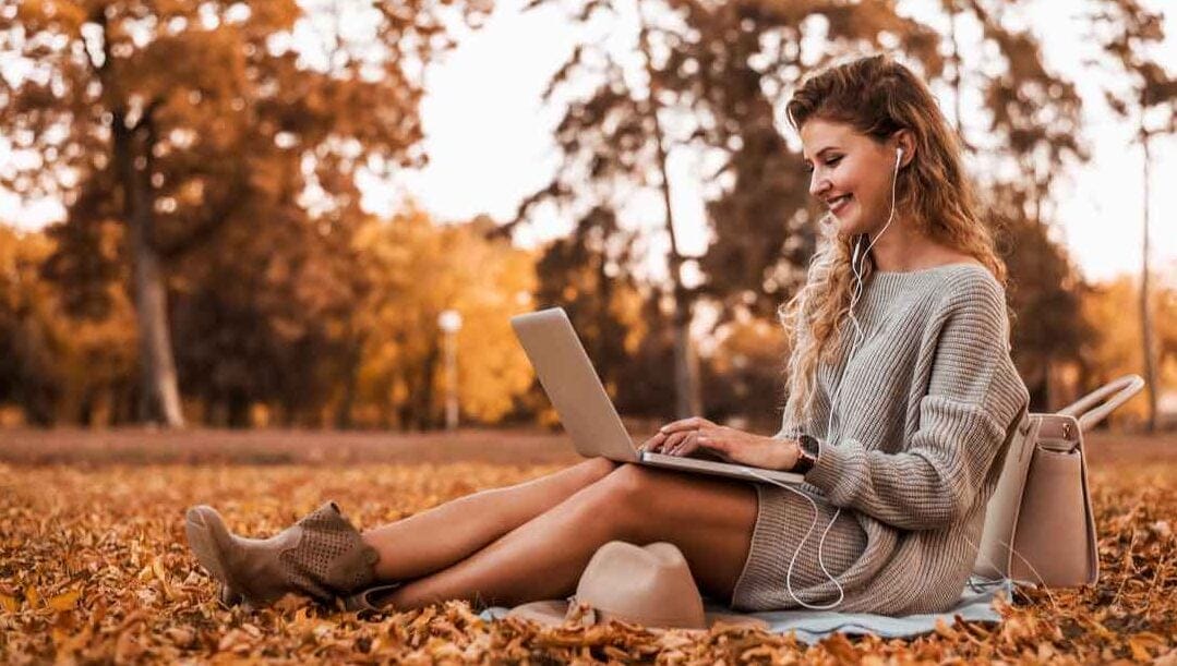 Side view of a woman using a laptop in a park during autumn.