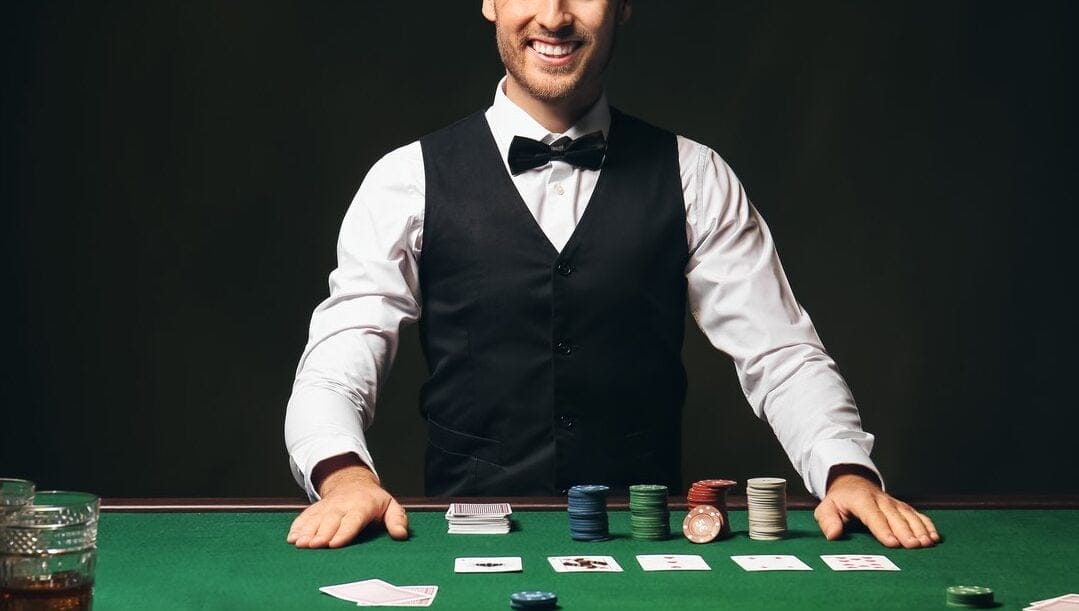 A croupier standing in front of a casino games table with chips and cards on the table.