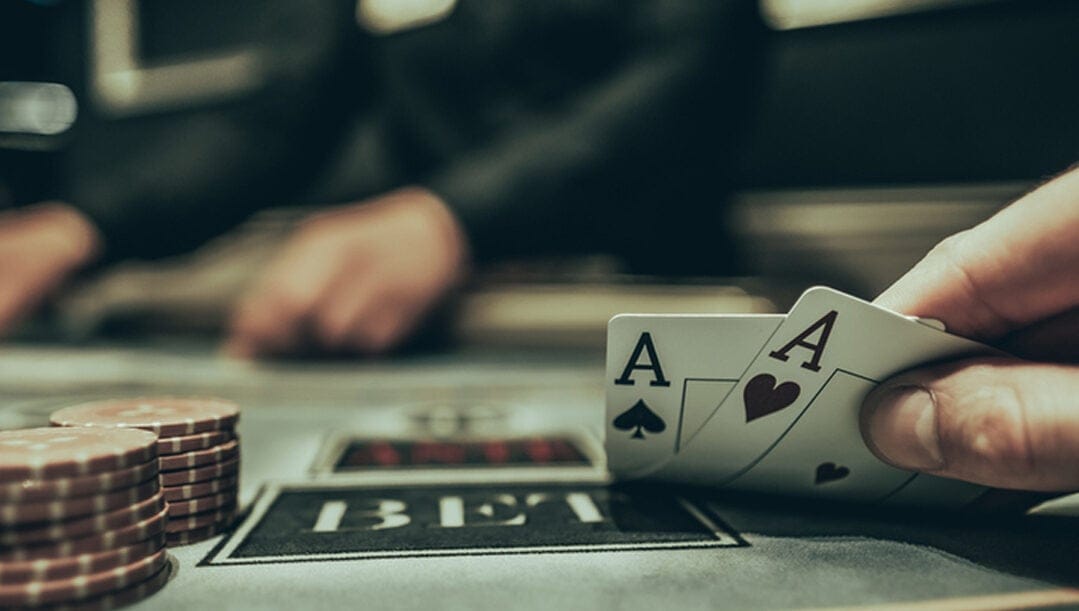 Close-up of a man’s hand lifting the corner of his cards to show two aces.