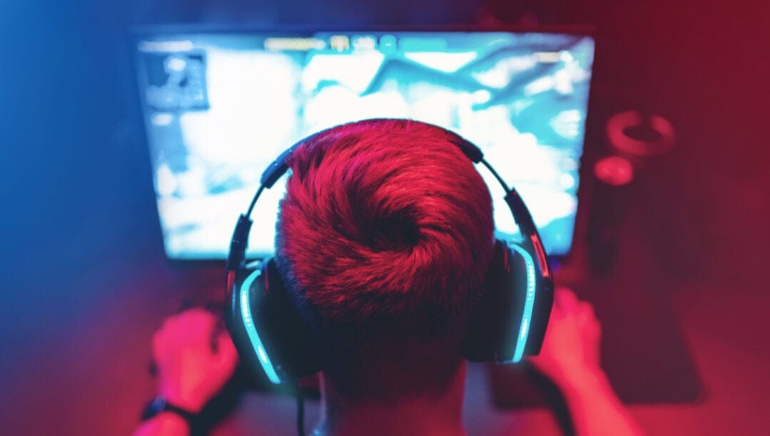Gamer playing on a desktop wearing a headset in a red-lit room.