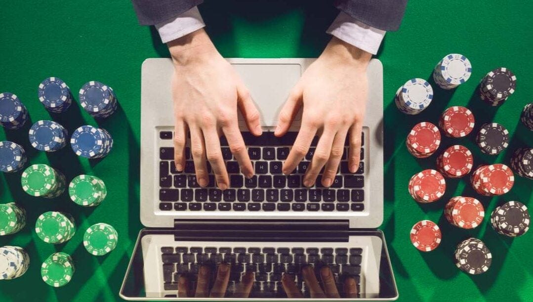 Hands on a laptop keyboard on a green felt table surrounded by colorful poker chips.