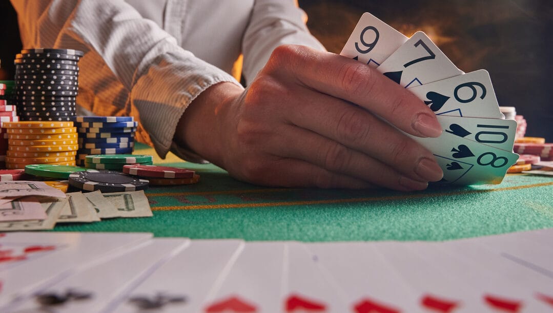 A dealer with chips next to him shows some cards on a poker table.