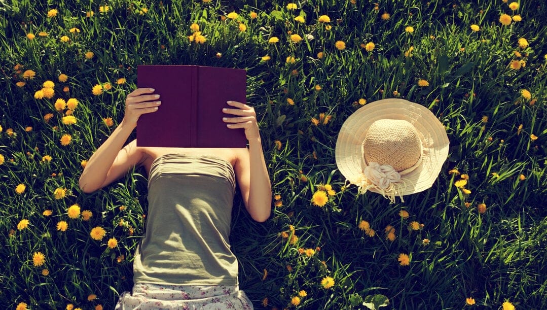 A woman lying in a field of flowers reading a book.