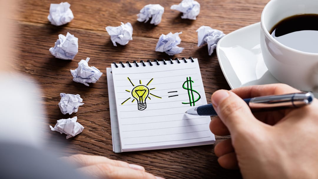 A man drawing an idea lightbulb and dollar sign on a notepad.