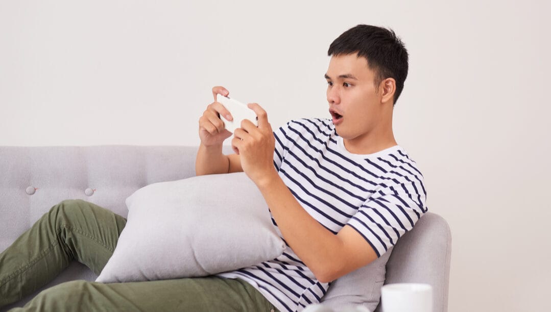 A man playing games on his phone and looking surprised.