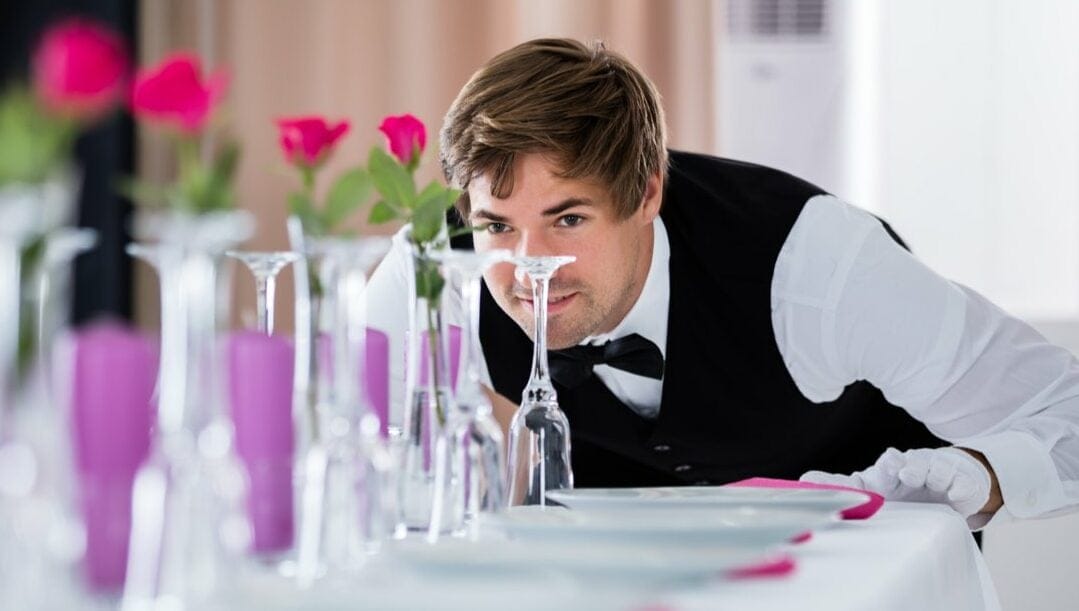 A waiter looking at glasses placed on a table.