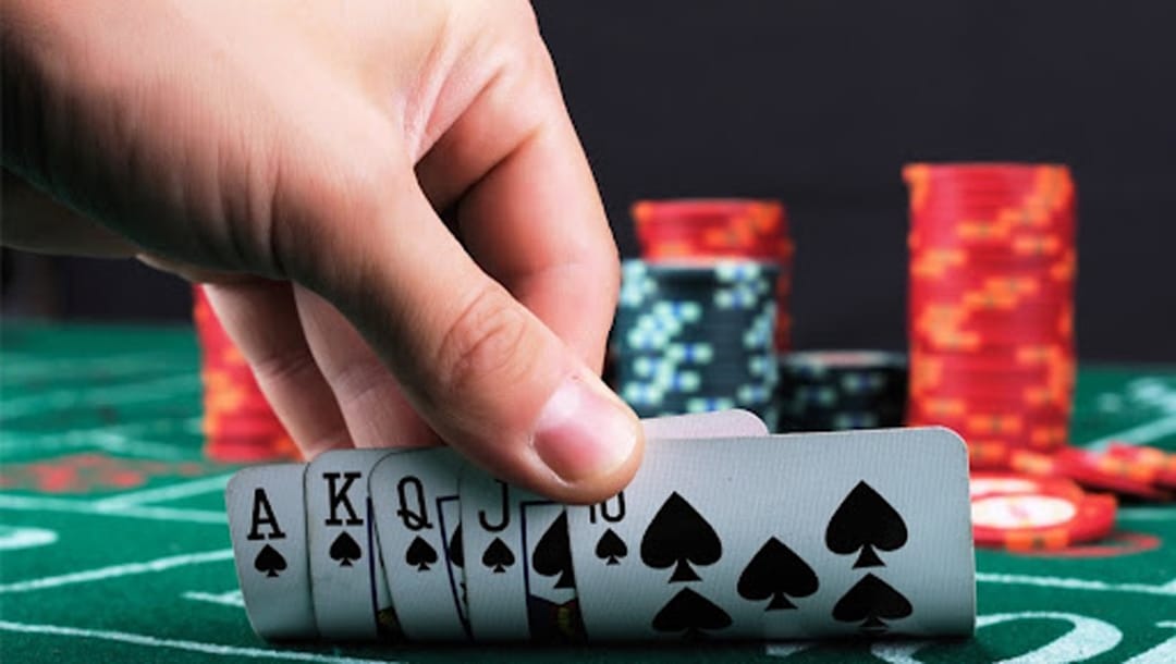 A hand revealing playing cards on a poker table with poker chips in the background.