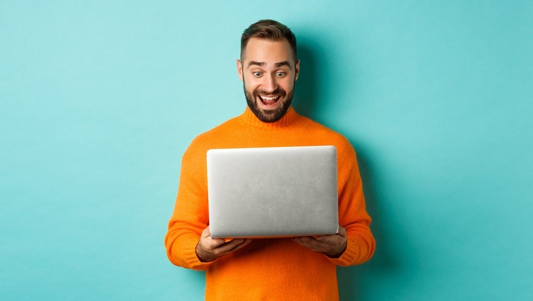 An excited man holding a laptop against an isolated turquoise background.