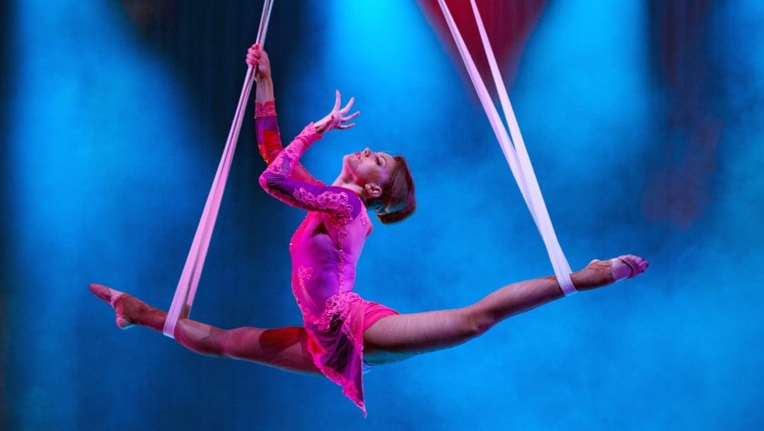 A woman does the splits between two silk ropes in the air.