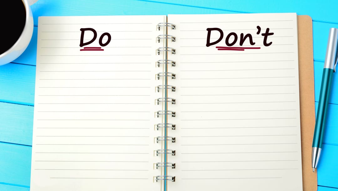 A notepad with “Do” and “Don’t” written on the pages with a pen and a cup of coffee on top of a blue table.