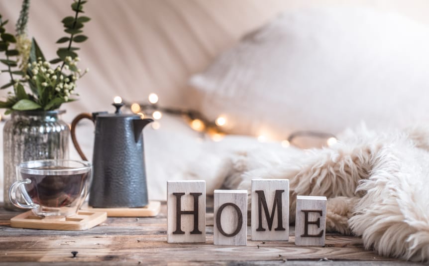 The word home spelled out in wooden blocks on a table beside a blanket and warm drink.