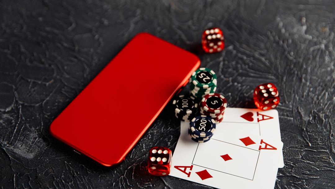 Smartphone on a table next to casino chips, dice and a pair of Aces.