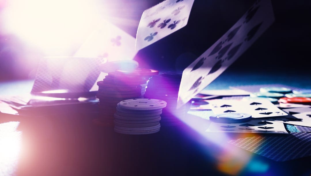 Table with casino chips and cards with a light shining onto it.